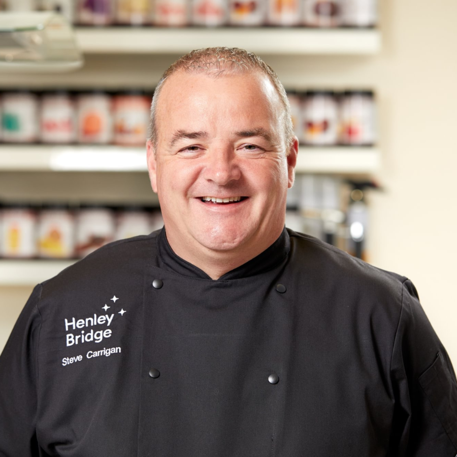 Steve Carrigan wearing a black chef's coat with 'Henley Bridge' branding in a kitchen setting.
